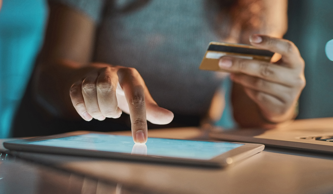 Una donna con la carta di credito in una mano clicca su un tablet per completare un acquisto online