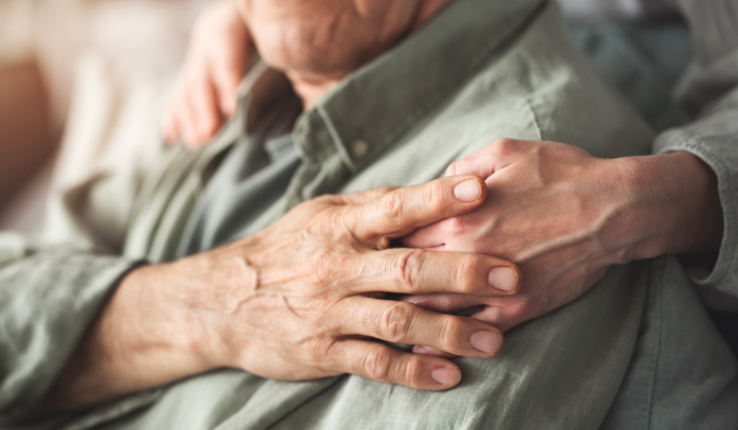 Long Term Care e tutela legale - La mano giovane del caregiver posata sulla spalla di un anziano. L'anziano stringe la mano del giovane