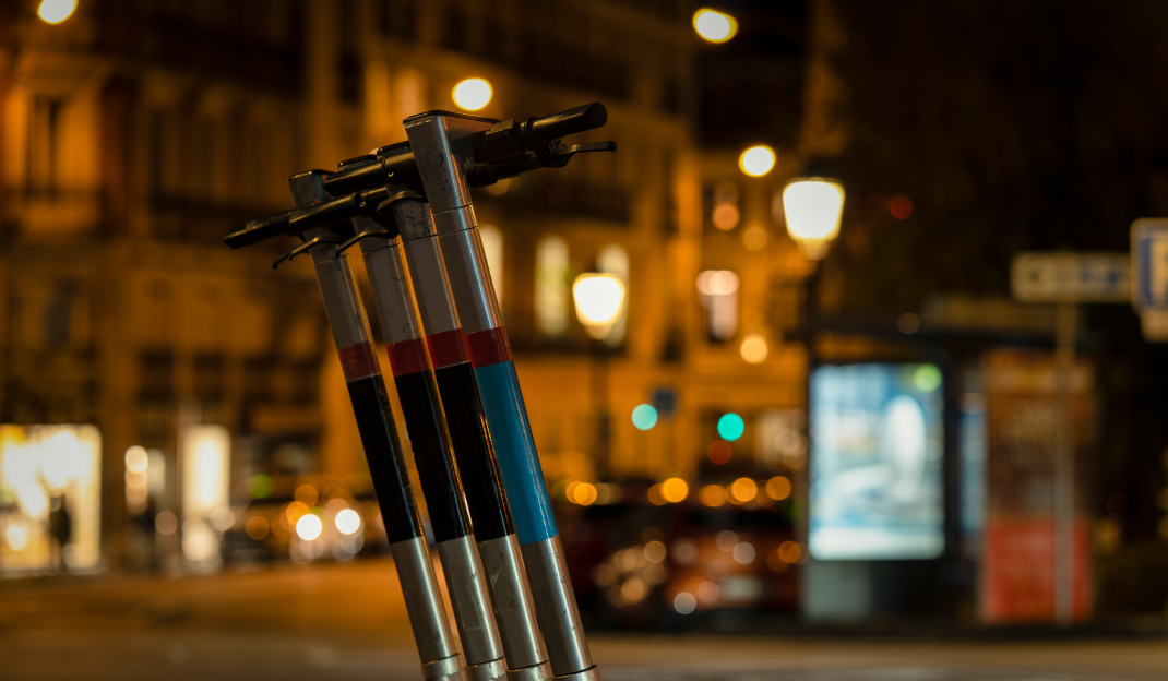 4 monopattini parcheggiati in fila sul marciapiede di una città illuminata dalle luci dei lampioni